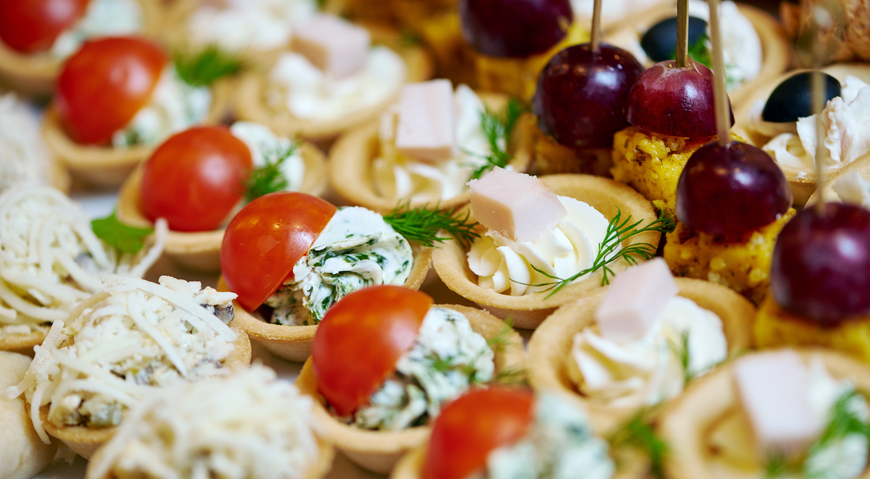 Primer plano de una selección de mini tartaletas con diversos ingredientes, como tomates y queso.