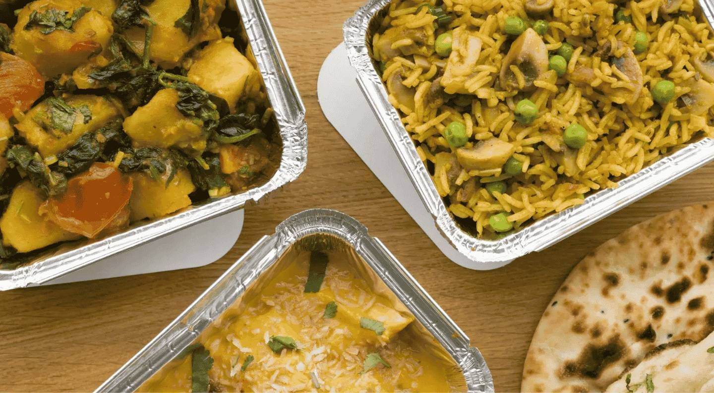 Comida india en envases de aluminio: curry de patatas, arroz con champiñones, un plato cremoso y pan naan.