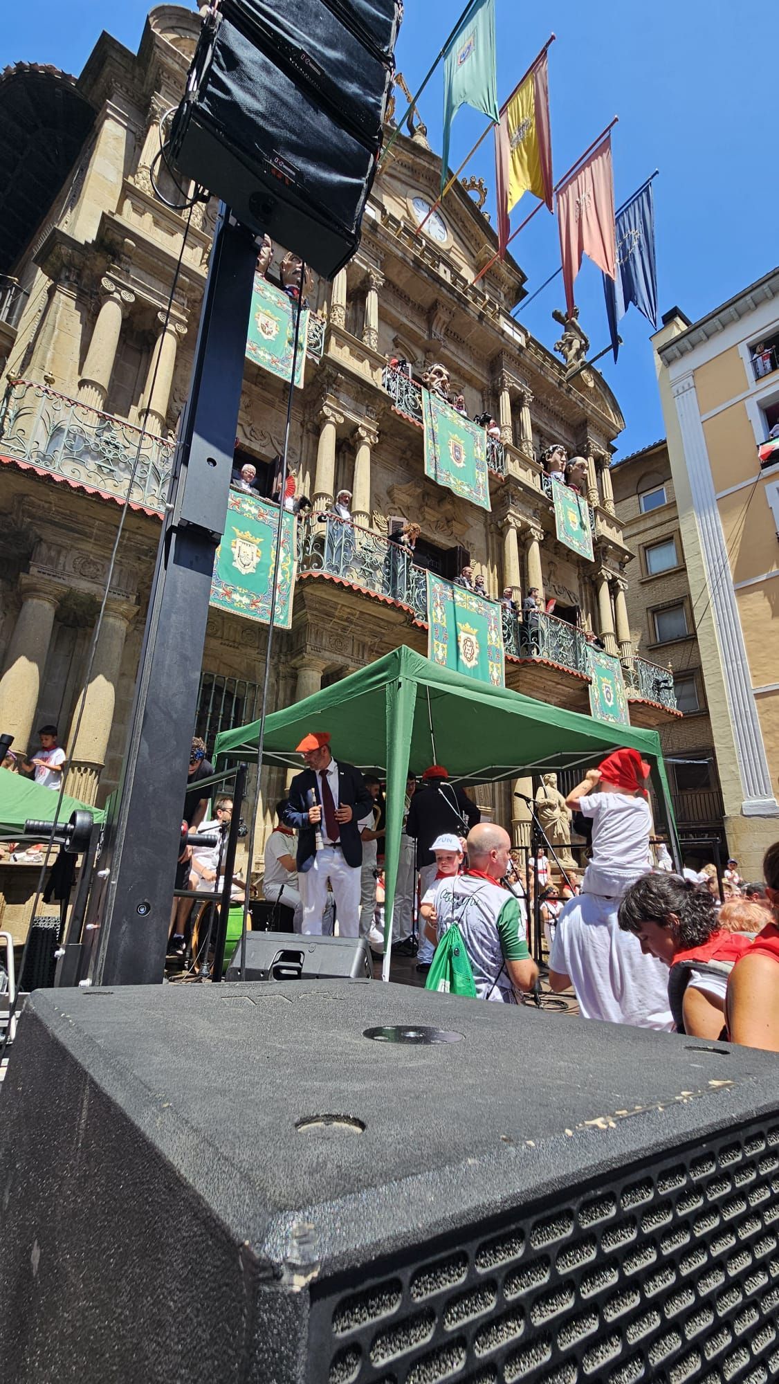 Un grupo de personas está de pie bajo una carpa verde frente a un edificio.