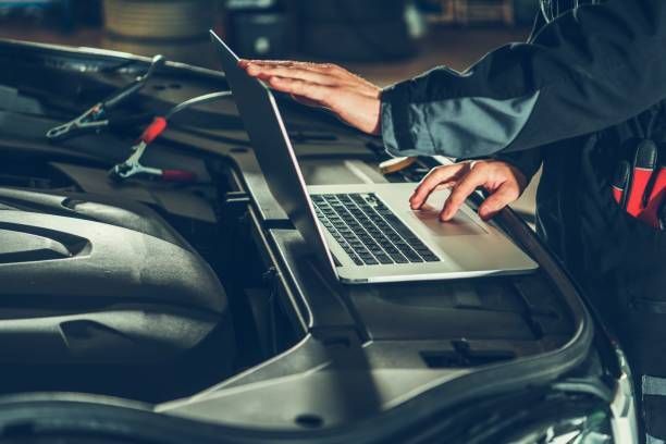 Un mecánico está usando una computadora portátil para revisar el motor de un automóvil.