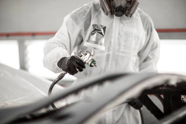 Un hombre con un traje protector está pintando con aerosol un automóvil.