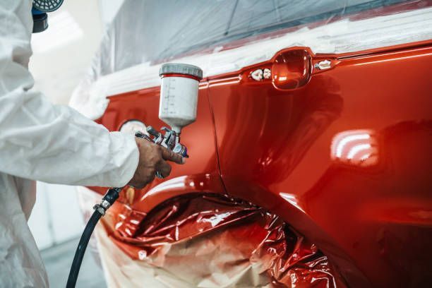 Un hombre está pintando con aerosol un coche rojo en un garaje.