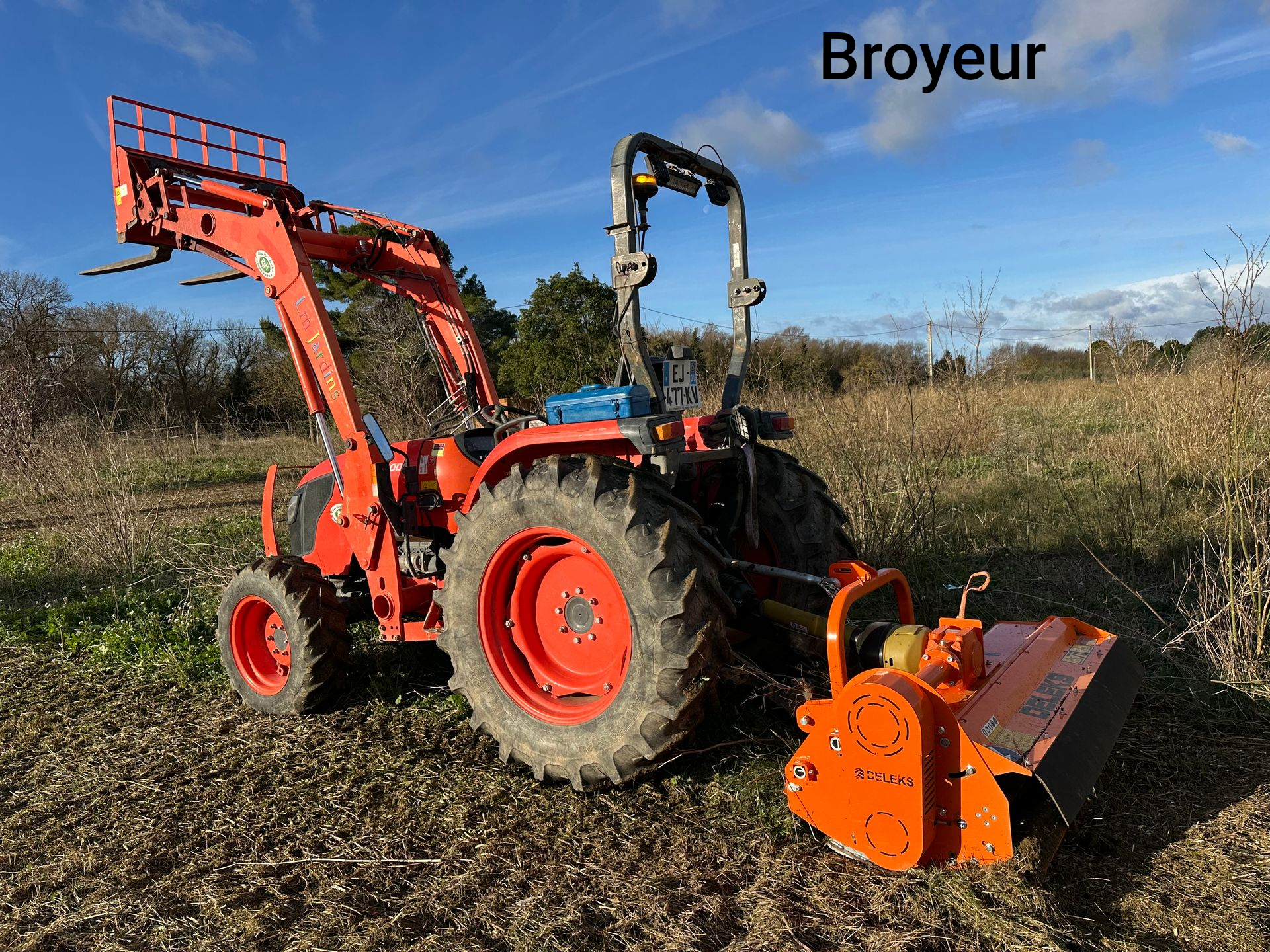 Tracteur orange avec chargeur et broyeur dans un champ.