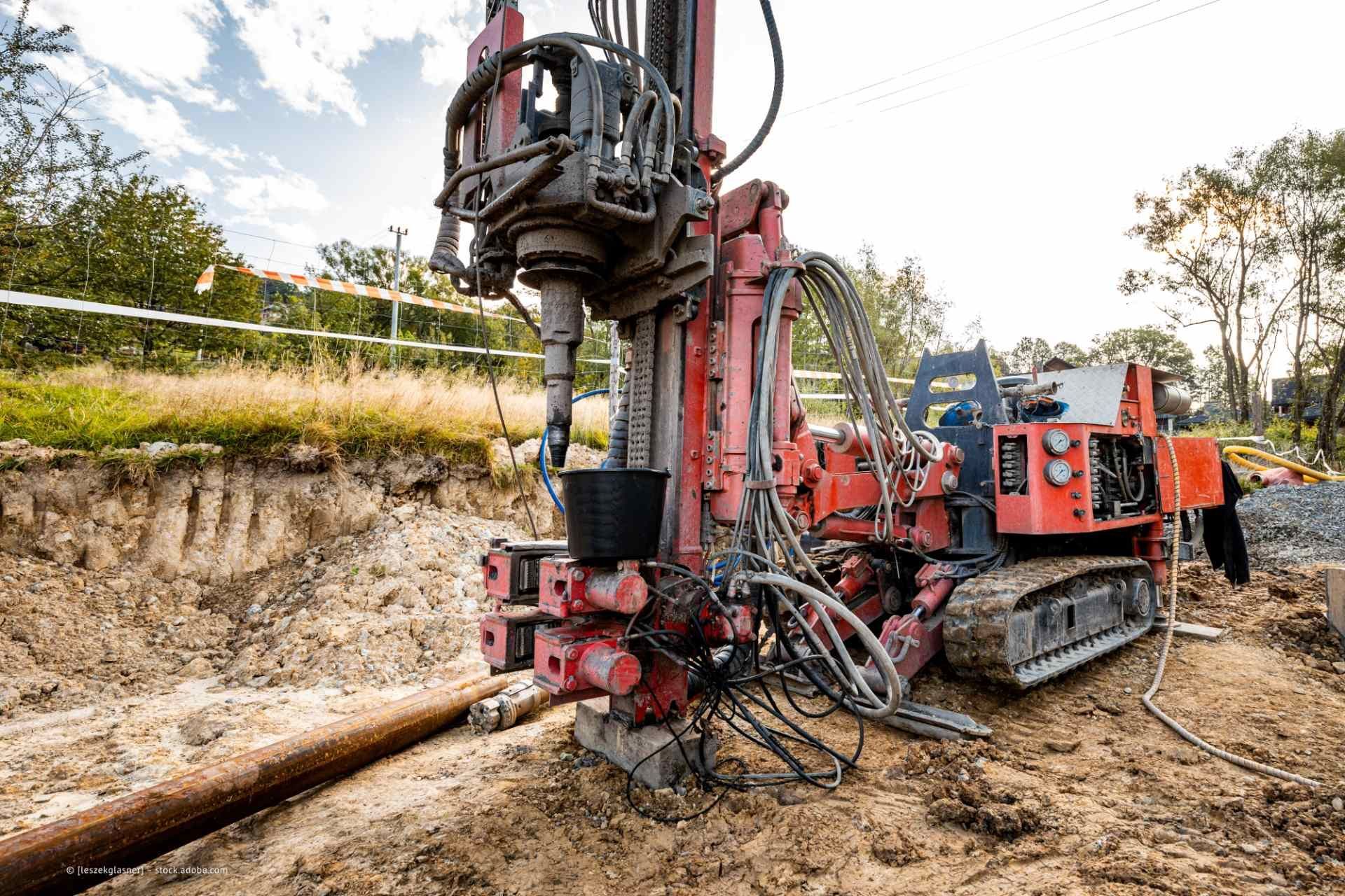 Rote Bohrmaschine beim Ausheben eines Grabens auf einer Baustelle im Freien.