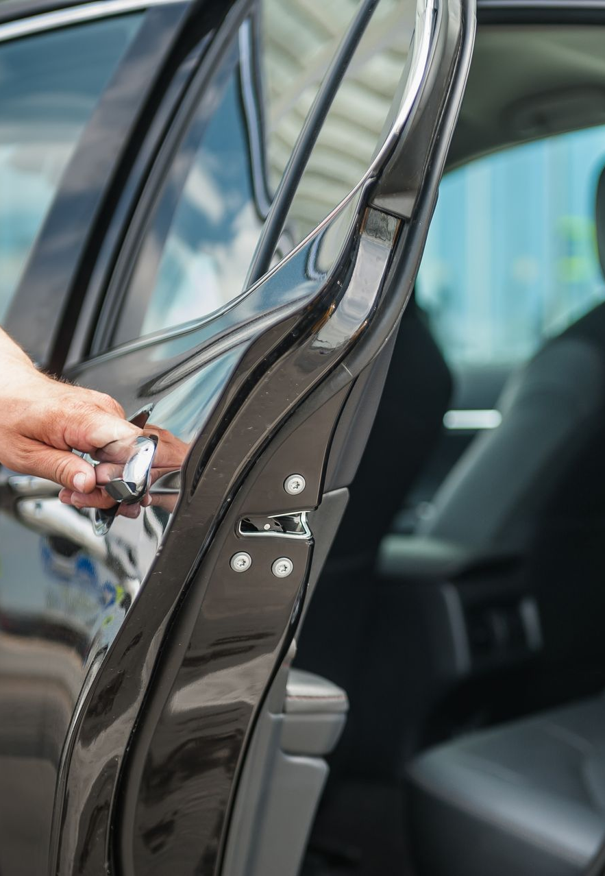 Portière de voiture noire entrouverte, main sur la poignée.