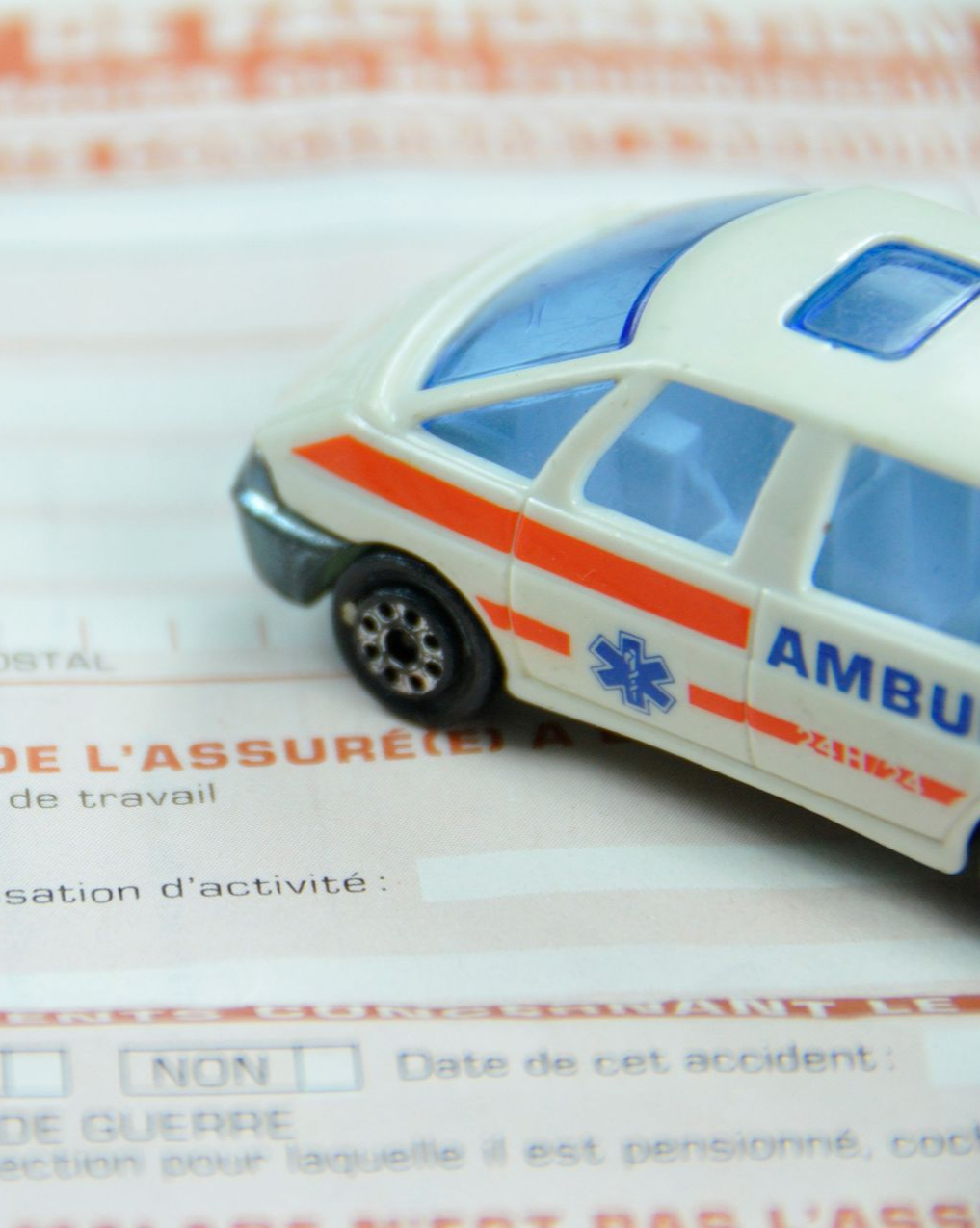 Ambulance miniature posée sur un formulaire ; bande orange, touches de bleu, symbole médical.