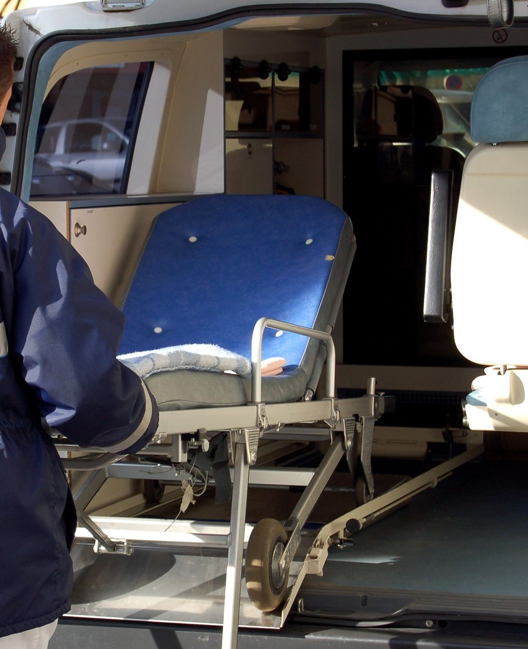 Une ambulance ouverte et une personne en sort un brancard bleu et argenté.
