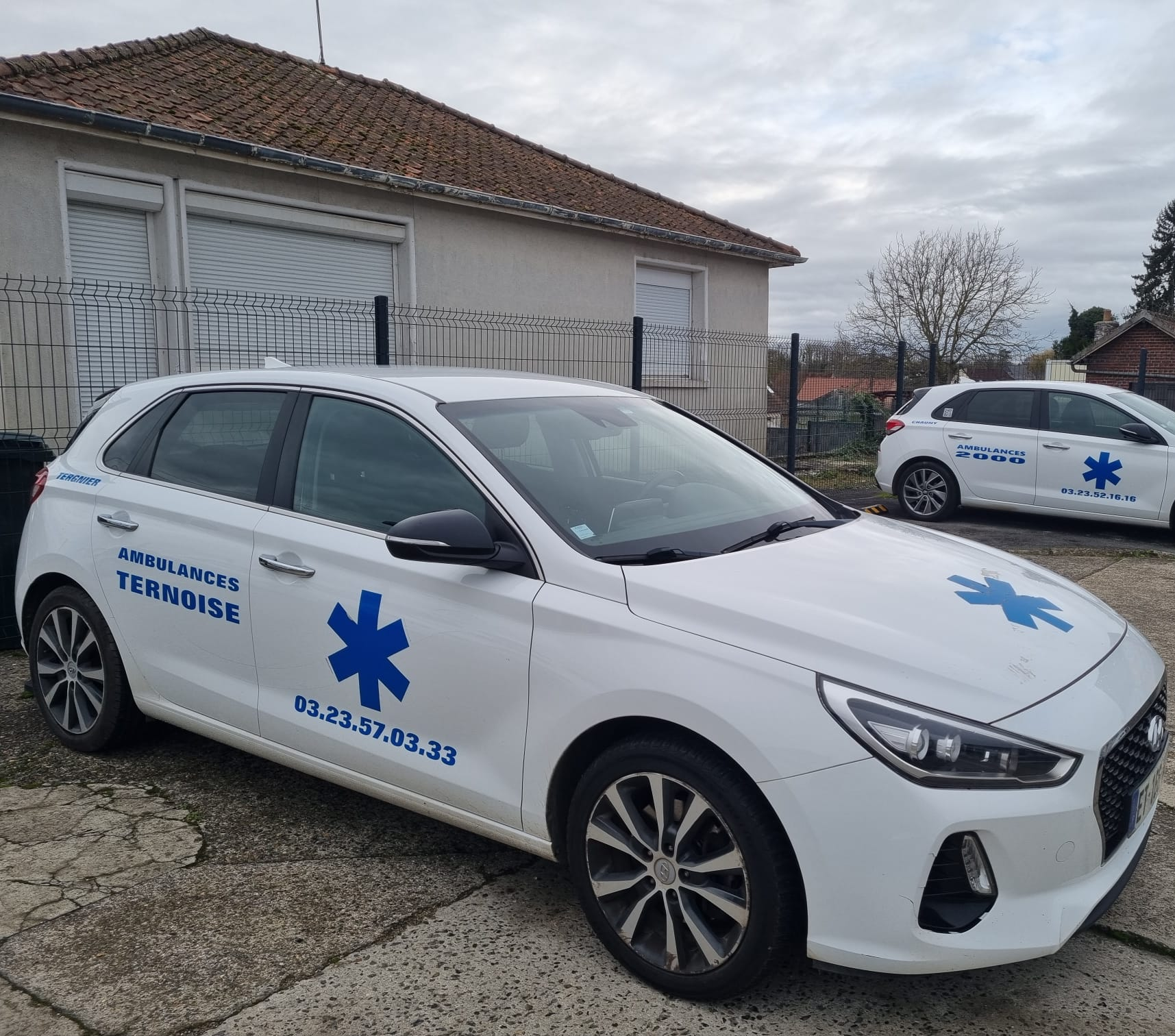 Voiture blanche avec des autocollants d'ambulance ; autres ambulances en arrière-plan.