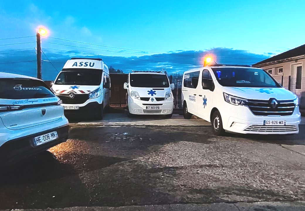 Des ambulances stationnées dans une rue mouillée au crépuscule, gyrophares allumés.