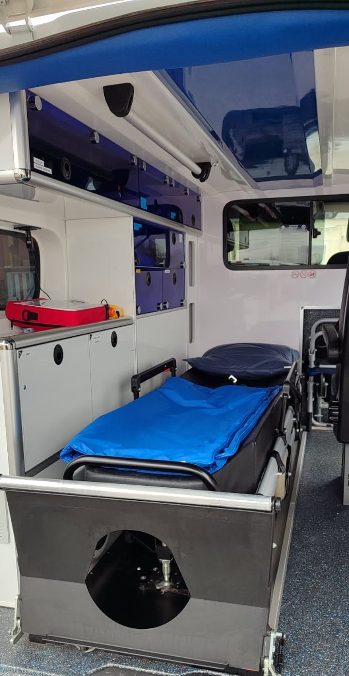 Intérieur d'une ambulance. On aperçoit une civière et des sièges, ainsi que du matériel médical.