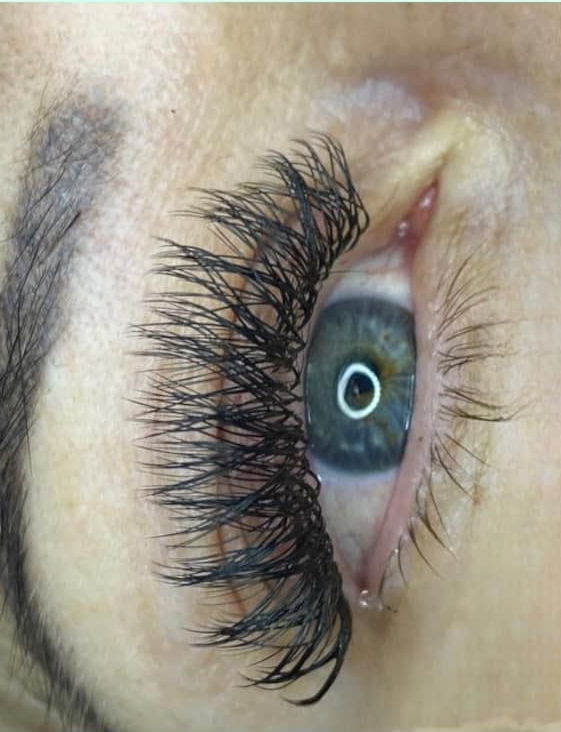 Primer plano de un ojo con extensiones de pestañas largas y oscuras, iris verde y ceja oscura.