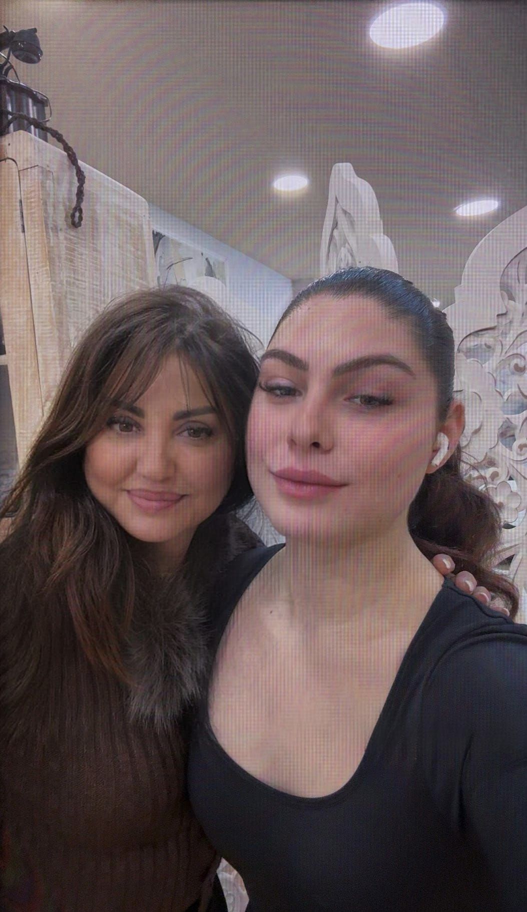 Dos mujeres sonriendo, abrazándose frente a la cara de una mujer de dibujos animados.