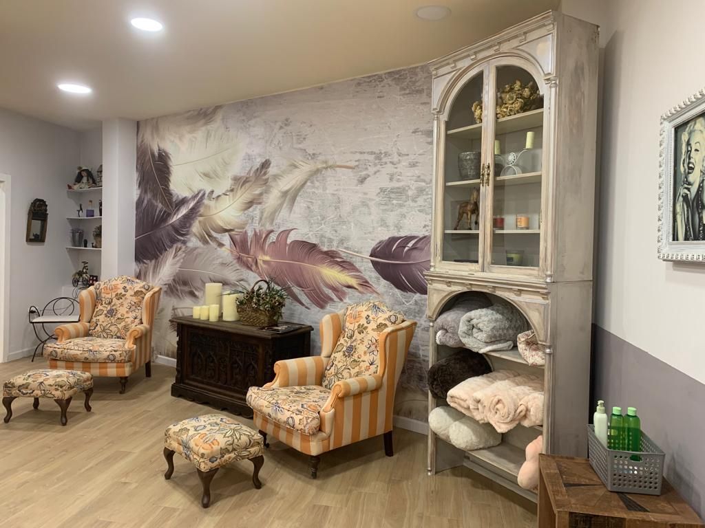 Acogedora sala de espera con sillones florales, reposapiés y un gran armario frente a una pared con mural de plumas.