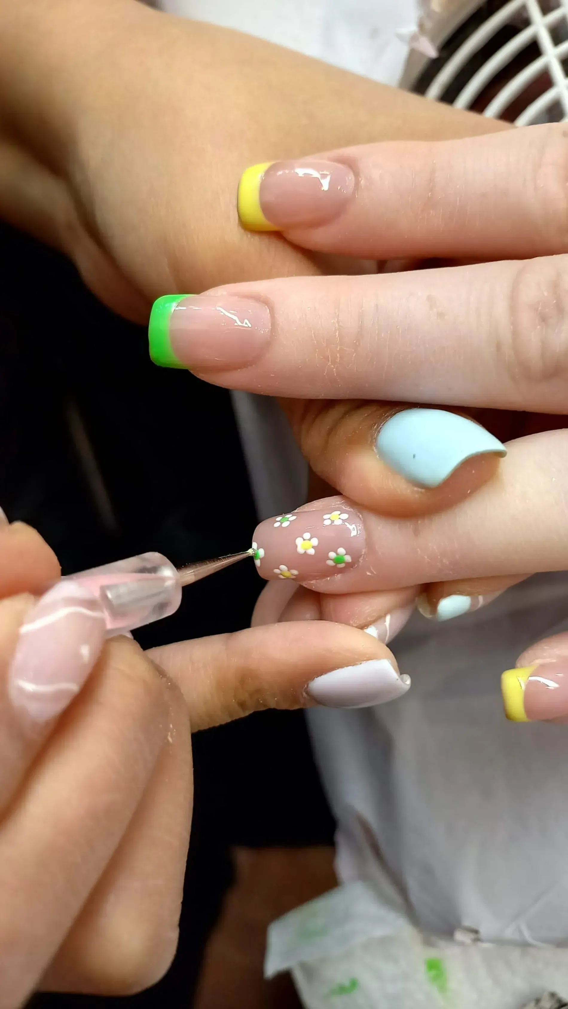Persona aplicando arte de uñas con pequeñas flores y puntas de colores.
