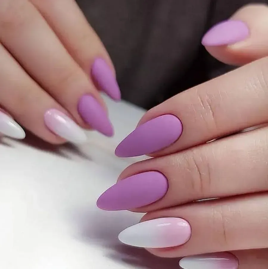 Manos con uñas en forma de almendra de color lavanda mate y blanco rosado ombré.