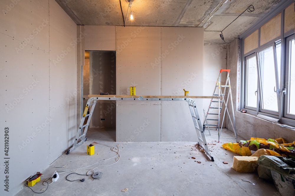 Teilweise renoviertes Zimmer mit Leitern, Gerüsten und Baumaterialien an grossen Fenstern