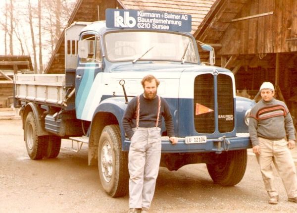 Zwei Männer stehen vor einem blauen Pritschenwagen in einem matschigen Hof.