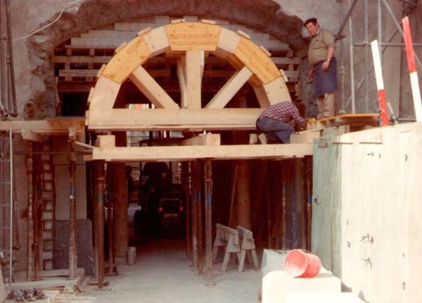 Arbeiter montieren einen grossen Holzbogen am Eingang einer steinernen Baustelle