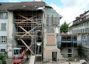 Altes Gebäude im Umbau mit Gerüst, freiliegenden Balken und einem Bagger davor