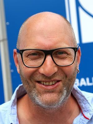 Lächelnder, glatzköpfiger Mann mit Brille in einem hellblauen Hemd vor blauem Hintergrund