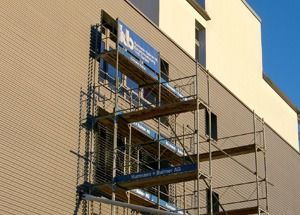 Ein Baugerüst neben einem beigen Gebäude unter blauem Himmel, mit einem blauen Schild in der Nähe der Spitze
