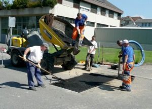 Arbeiter reparieren mit einem kleinen Bagger und Werkzeugen eine Strasse in der Nähe eines Hauses.