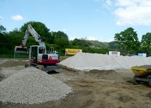 Baustelle mit Bagger, Kieshaufen und Muldenkippern unter blauem Himmel