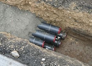 Drei schwarze Artilleriegranaten mit roten Streifen liegen in einem Erdgraben.