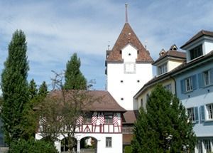 Historische Gebäude am Hang mit weissen und blauen Fassaden, Bäume und ein hoher Turm unter blauem Himmel