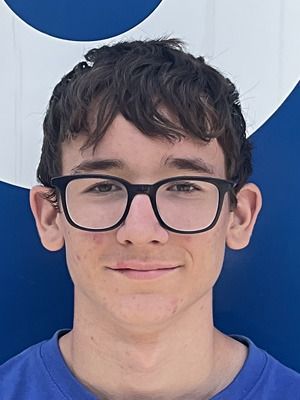 Junger Mensch mit schwarzer Brille und zerzaustem Haar, der ein blaues Hemd trägt, vor einem blau-weissen Hintergrund