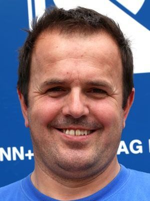 Lächelnder Mann in einem blauen Hemd vor einem blauen Hintergrund mit weissem Text