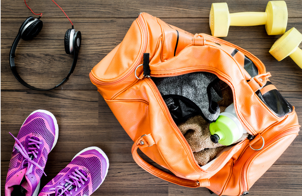Una borsa da viaggio piena di vestiti, scarpe, cuffie e manubri su un pavimento di legno.