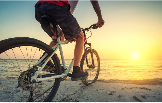 Un uomo sta andando in bicicletta sulla spiaggia al tramonto.
