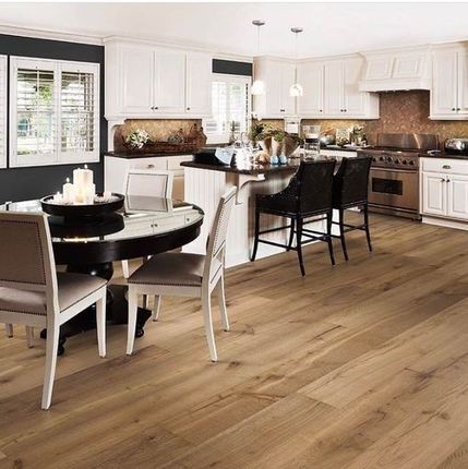 Cocina y comedor modernos y luminosos con armarios blancos, suelos de madera y taburetes de bar negros.