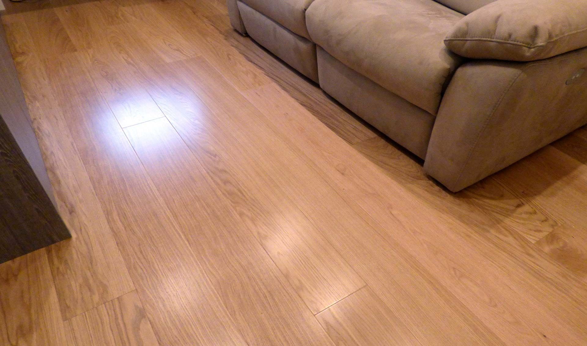 Salón con suelo de madera, sofá modular beige y un brillante reflejo de luz.