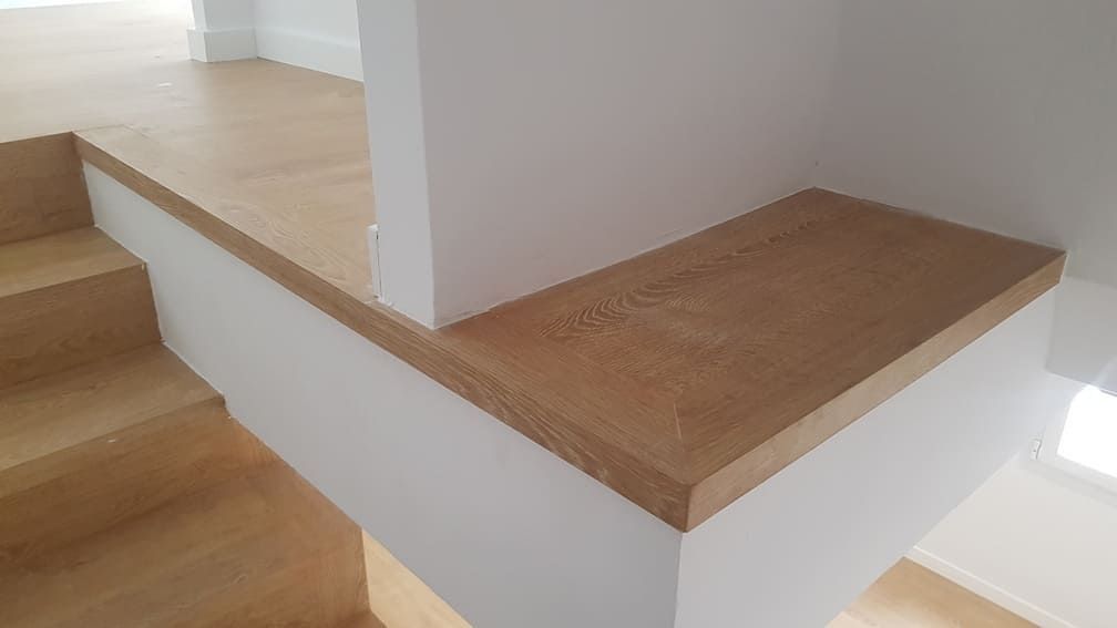 Rellano de escalera de madera con banco esquinero incorporado y paredes blancas en un interior luminoso.