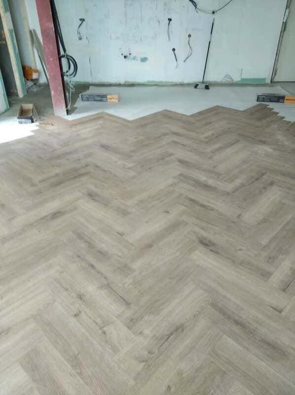 Suelo de madera con diseño de espiga en una habitación en construcción con paredes sin terminar.