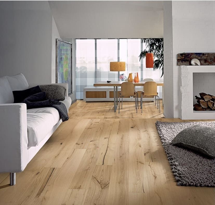 Sala de estar moderna con suelos de madera clara, sofá gris, mesa de comedor y una gran pared con ventanal.