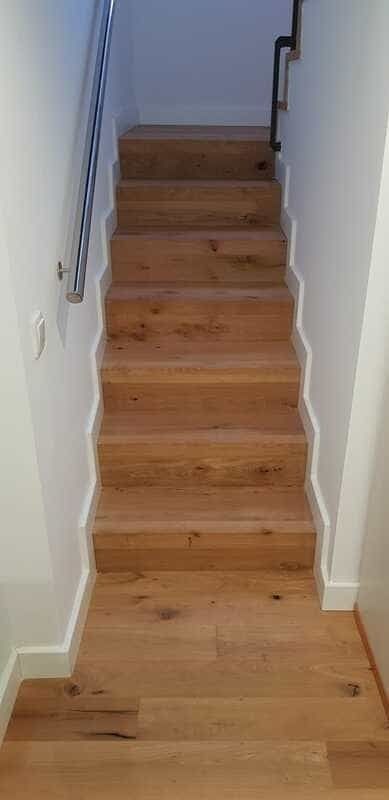 Escalera de madera con paredes estrechas blancas y un rellano con suelo de madera clara en la parte superior.