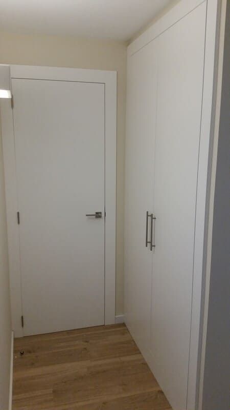Pasillo estrecho con puertas blancas, paredes blancas y suelo de madera clara.