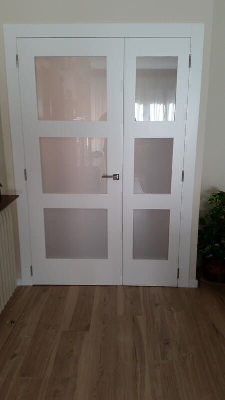 Puertas dobles de cristal blancas en un pasillo con suelo de madera clara.