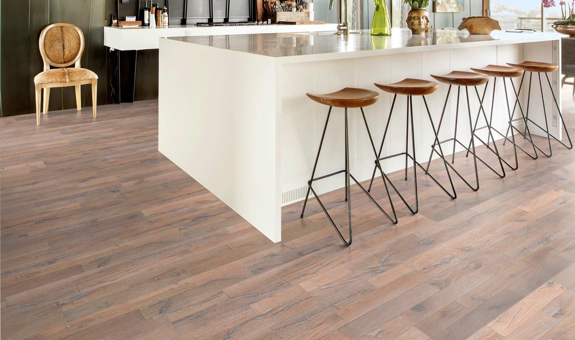 Cocina moderna con isla blanca, taburetes de madera y suelo de madera rústica.