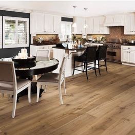 Cocina moderna y luminosa con armarios blancos, suelos de madera, taburetes negros en la isla y una mesa de comedor redonda.