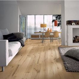 Salón moderno con suelos de madera clara, sofá blanco, mesa de comedor y chimenea cerca de grandes ventanales.
