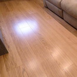 Suelo de madera clara brillante junto a un sofá beige en una sala de estar.