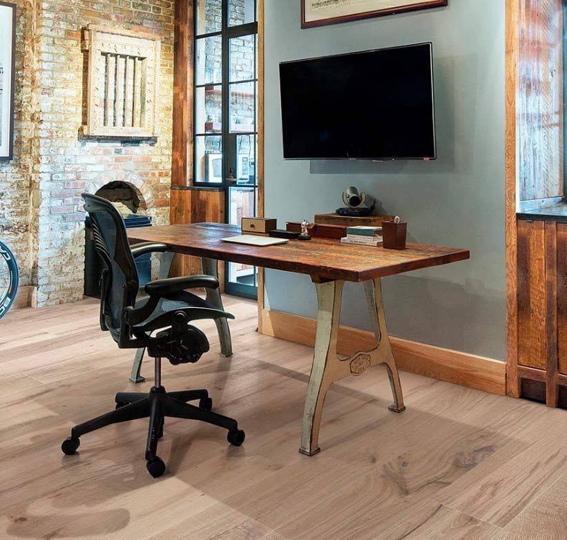 Oficina en casa con escritorio, silla negra, televisor montado en la pared y detalles de ladrillo visto.