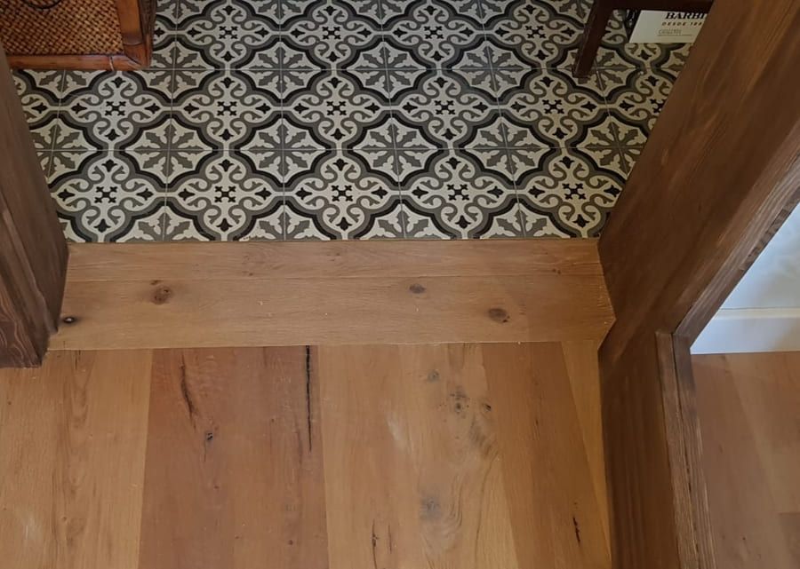 Umbral de madera en la entrada, entre un suelo de madera clara y un suelo de baldosas estampadas.