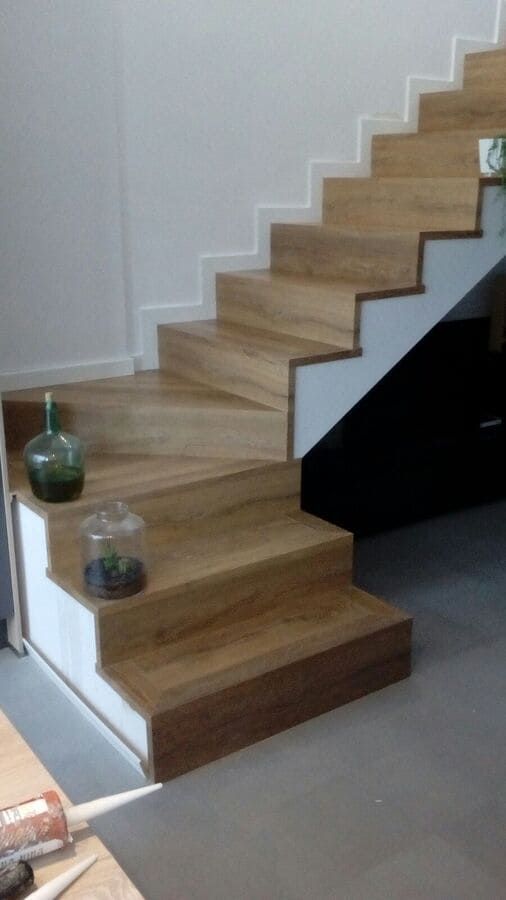 Escalera de madera con paredes blancas y un panel lateral negro en un interior moderno.