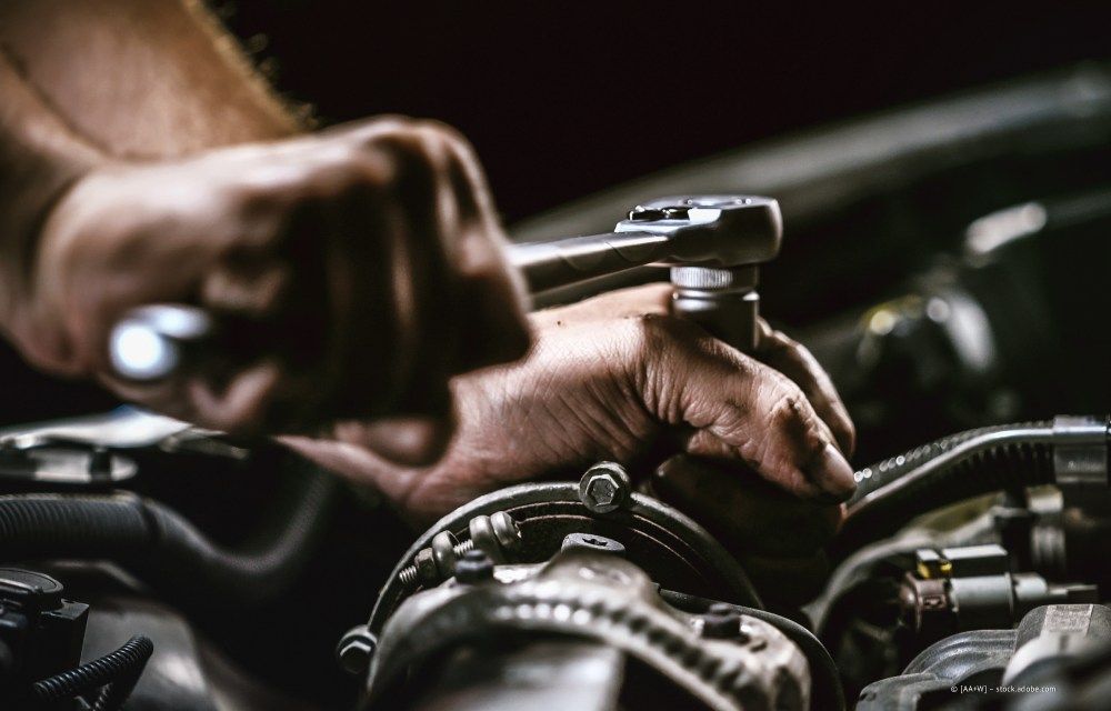 Hände benutzen einen Schraubenschlüssel, um in einer Garage einen Automotor zu reparieren