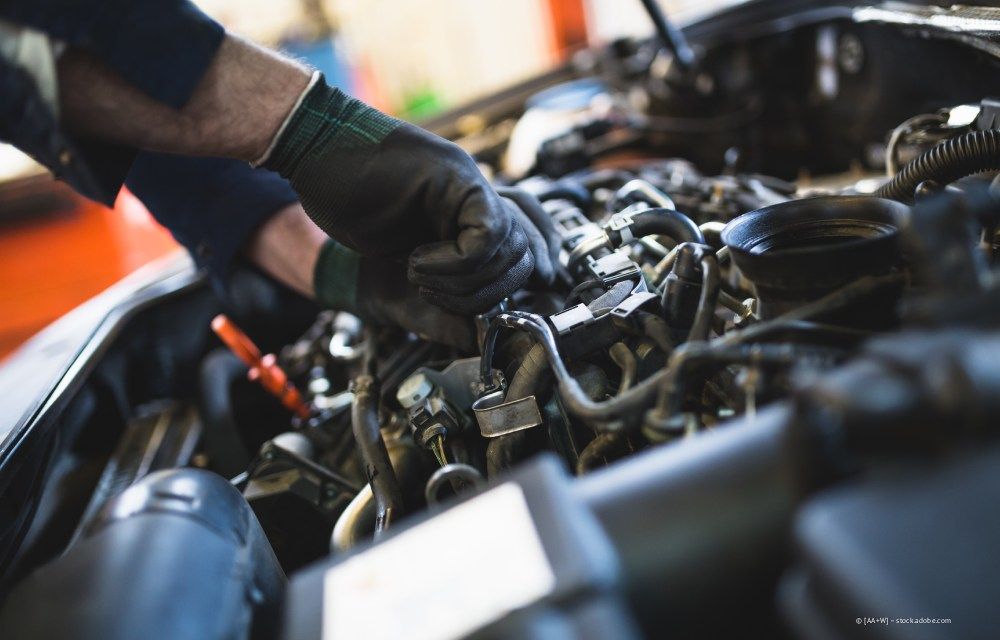Die behandschuhten Hände eines Mechanikers arbeiten in einer Garage an einem Automotor.